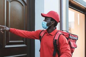 Afrikaanse rijder Mens leveren maaltijd naar klanten huis terwijl vervelend gezicht masker gedurende corona virus het uitbreken - levering voedsel concept foto