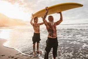 gelukkig vrienden met verschillend leeftijd surfing samen Aan tropisch oceaan - sportief mensen hebben pret gedurende vakantie surfen dag - ouderen en jeugd mensen en extreem sport levensstijl concept foto