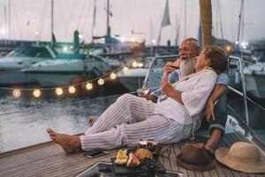 senior paar drinken Champagne en aan het eten tropisch fruit Aan zeilboot vakantie - volwassen mensen hebben pret vieren bruiloft verjaardag Aan boot reis - liefde verhouding en reizen levensstijl concept foto