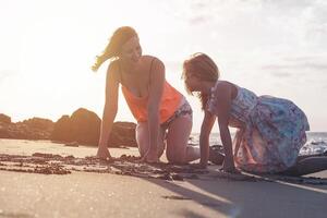 moeder en dochter hebben pret tekening met zand Bij zonsondergang Aan tropisch strand - gelukkig mam spelen met haar kind in vakantie - liefde, geluk en familie levensstijl concept foto