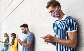 jong mensen vervelend gezicht masker gebruik makend van mobiel smartphone buitenshuis - multiraciaal vrienden hebben pret met nieuw technologie sociaal media app gedurende corona virus het uitbreken - jeugd millennial levensstijl concept foto