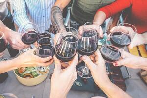 gelukkig familie roosteren met rood wijn bril Bij avondeten buitenshuis - mensen hebben pret juichen en drinken terwijl dining samen - voedsel en drank weekend levensstijl activiteiten foto