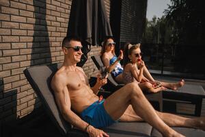 een gelukkig familie in zwemkleding zonnebaden in zomer Aan hun terras Aan zon bedden foto