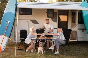 een gelukkig familie is resting dichtbij in de buurt hun camper in de Woud foto