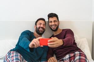 gelukkig homo paar hebben pret gebruik makend van mobiel smartphone in bed - homoseksueel liefde en technologie concept foto