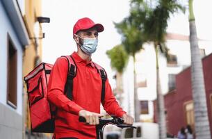 rijder Mens leveren maaltijd met elektrisch scooter in de stad terwijl vervelend gezicht masker gedurende corona virus het uitbreken - ecologisch snel levering voedsel concept foto