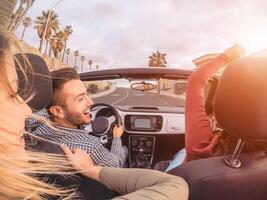 gelukkig vrienden hebben pret Aan converteerbaar auto gedurende weg reis - groep modieus jong mensen genieten van vakantie samen in tropisch stad - jeugd cultuur levensstijl en reizen vervoer concept foto