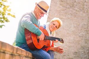 gelukkig senior paar spelen een gitaar en hebben een romantisch datum buitenshuis - volwassen mensen hebben pret genieten van tijd samen in vakantie - concept van ouderen levensstijl activiteiten foto