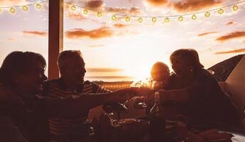 gelukkig senior vrienden juichen en roosteren met rood wijn Bij terras avondeten - volwassen mensen hebben pret dining samen Aan op het dak Bij zonsondergang - vriendschap, voedsel en drankje, ouderen levensstijl concept foto