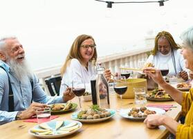 multiraciaal senioren dining samen Bij huis terras - ouderen mensen hebben Bij avondeten Aan huis patio - voedsel en drinken concept foto