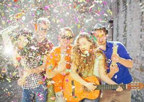 jong vrienden hebben een groot straat partij - groep van gelukkig mensen het werpen confetti, spelen gitaar, het zingen en dansen Aan de straat - focus Aan confetti foto