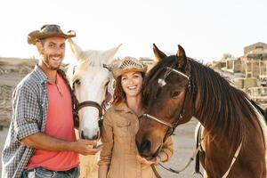 gelukkig paar hebben pret met paarden binnen stal - jong boeren sharing tijd met dieren in corral boerderij - menselijk en dieren verhouding levensstijl concept foto