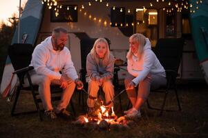 een familie kookt worstjes Aan een vreugdevuur in de buurt hun camper in de bossen foto