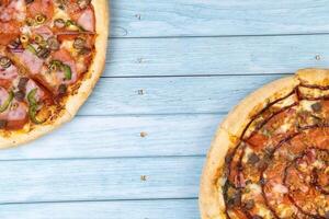 twee verschillend heerlijk groot pizza's Aan een blauw houten achtergrond foto