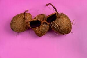 drie geheel kokosnoten en houten bril Aan een roze achtergrond foto