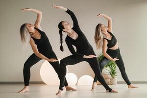 een groep van meisjes in zwart aan het doen yoga poses binnenshuis. Dames zijn verloofd in geschiktheid foto