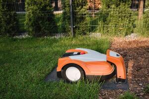 een oranje robot gazon maaier staat Aan de baseren en is opgeladen van elektriciteit in de binnenplaats foto