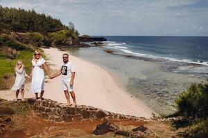 een familie in wit met drie mensen looks in de afstand van gris gris strand Aan de eiland van Mauritius. de familie looks Bij de mooi natuur van de eiland van Mauritius en de Indisch oceaan foto