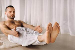 een Mens met een kaal torso doet yoga in een geschiktheid kamer. de concept van een gezond levensstijl foto