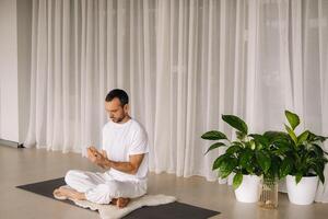 een Mens in wit sportkleding is aan het doen yoga met een geschiktheid kamer. de concept van een gezond levensstijl foto