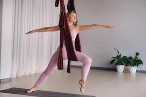 een vrouw in roze kleren doet yoga Aan een geschorst bordeaux hangmat in een helder Sportschool foto