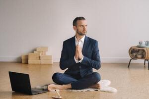 een Mens in een formeel pak mediteert terwijl zittend in een geschiktheid kamer met een laptop foto
