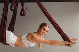 een meisje in wit sportkleding doet yoga Aan een hangende hangmat in de geschiktheid kamer foto