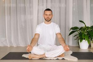 een Mens in wit sportkleding is aan het doen yoga met een geschiktheid kamer. de concept van een gezond levensstijl foto