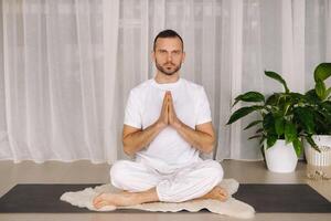 een Mens in wit sportkleding is aan het doen yoga met een geschiktheid kamer. de concept van een gezond levensstijl foto