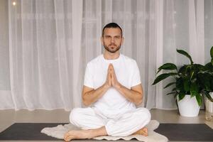 een Mens in wit sportkleding is aan het doen yoga met een geschiktheid kamer. de concept van een gezond levensstijl foto