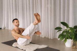 een Mens met een kaal torso doet yoga in een geschiktheid kamer. de concept van een gezond levensstijl foto