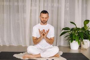 een Mens in wit sportkleding is aan het doen yoga met een geschiktheid kamer. de concept van een gezond levensstijl foto