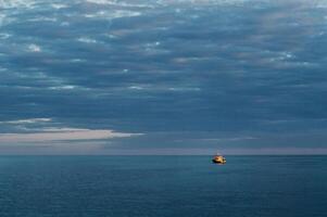 een klein schip Bij zee tegen de zonsondergang lucht foto