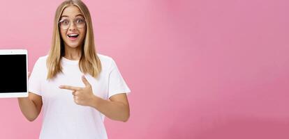 meisje suggereert kopen digitaal tablet voor Universiteit en vergeten papier boeken. opgewonden gelukkig en verheugd jong vrouw leerling in wit t-shirt en bril richten Bij apparaat scherm aanbevelen apparaatje foto