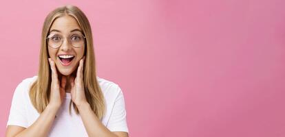 vrouw leuk vinden nieuw bril geplukt in op te slaan gevoel gelukkig vinden Rechtsaf kader aanraken wangen van geluk glimlachen vrolijk Bij camera vervelend transparant eyewear en t-shirt over- roze muur foto