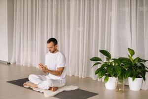 een Mens in wit sportkleding is aan het doen yoga met een geschiktheid kamer. de concept van een gezond levensstijl foto