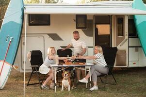 een gelukkig familie is resting dichtbij in de buurt hun camper in de Woud foto