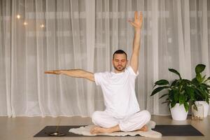 een Mens in wit sportkleding is aan het doen yoga met een geschiktheid kamer. de concept van een gezond levensstijl foto