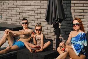 een gelukkig familie in zwemkleding zonnebaden in zomer Aan hun terras Aan zon bedden foto