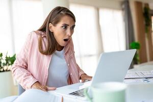 geschokt vrouw , uitgeput van werken aan het studeren moeilijk. verveeld en gefrustreerd op zoek Bij laptop. hoofd resting Aan hand. helder ruimte groot ramen. Bij huis concept. spanning concept. foto