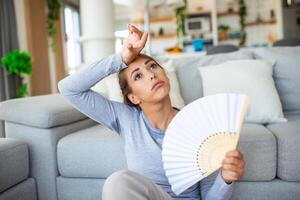 benadrukt geërgerd vrouw gebruik makend van golvend ventilator lijden van oververhitting, zomer warmte Gezondheid hormoon probleem, vrouw zweet voelen ongemakkelijk heet in zomer weer probleem zonder lucht conditioner foto