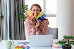 vrolijk youn vrouw ontwerper hebben video conferentie met klanten, zittend Bij bureau in voorkant van computer, Holding kleur paletten, gebaren en lachend, kopiëren ruimte foto