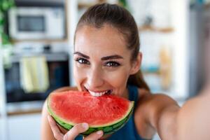 jong vrouw eet een plak van watermeloen in de keuken. portret van jong vrouw genieten van een watermeloen. foto
