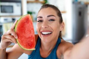 jong vrouw eet een plak van watermeloen in de keuken. portret van jong vrouw genieten van een watermeloen. foto