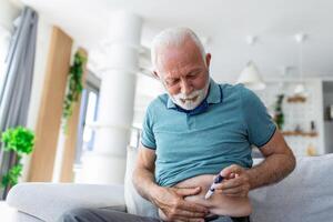 senior Mens zittend Aan sofa en geven zichzelf een insuline injectie voor zijn diabetes foto