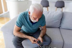 volwassen Mens testen voor hoog bloed suiker. Mens Holding apparaat voor meten bloed suiker, aan het doen bloed suiker testen. senior Mens controle bloed suiker niveau door glucometer en test streep Bij huis foto