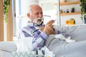 ziek ouderen Mens controle zijn temperatuur lijden van seizoensgebonden griep of verkoudheid aan het liegen Aan sofa vangen lijden van seizoensgebonden griep of koud. . ziek senior voelen ongezond met influenza Bij huis foto