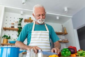 gelukkig gepensioneerd senior Mens Koken in keuken. pensioen, hobby mensen concept. portret van glimlachen senior Mens snijdend groenten foto