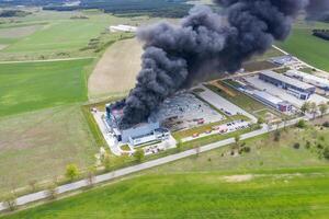antenne visie van verbrand industrieel magazijn of logistiek centrum gebouw na groot brand met reusachtig rook van verbrand dak foto