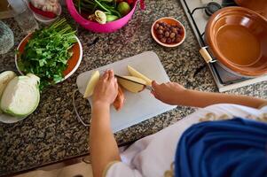 top visie huisvrouw hakken biologisch aardappel en groenten terwijl Koken tajine volgens naar traditioneel Marokkaans recept foto